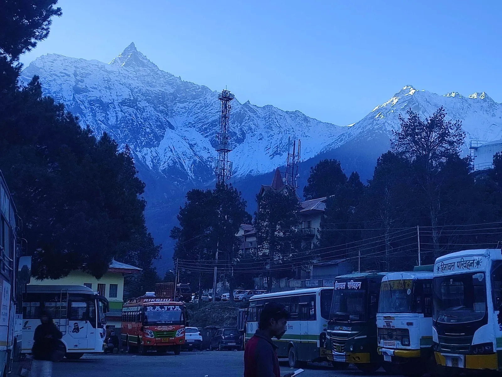 Reckong Peo bus stand at dusk with HRTC buses and snow peaks of the Kinner Kailash range above